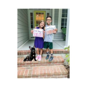 A girl and a boy standing on steps holding a first day of school sign with a dog for first day of school picture