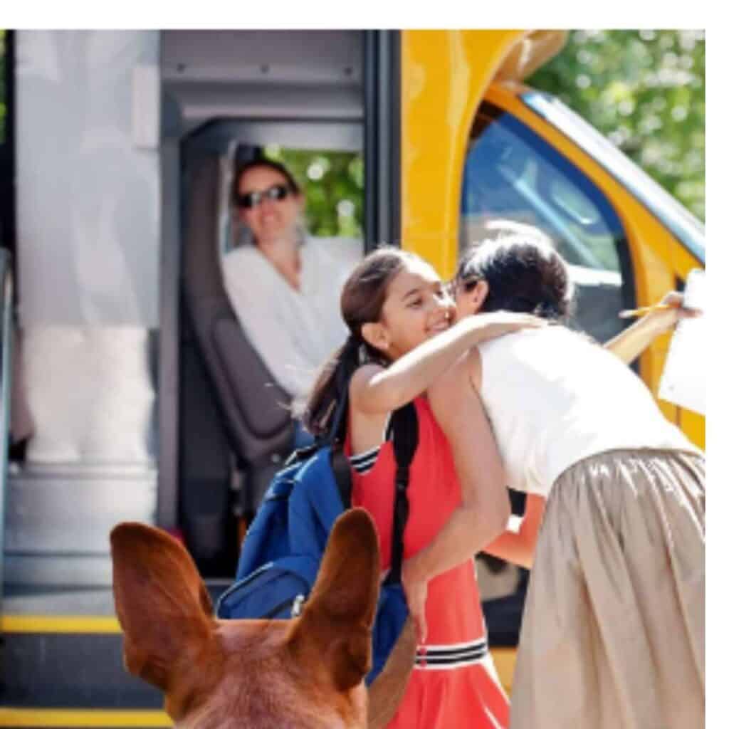 Dog looking on while a child gets on a school bus.