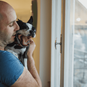 man looking out the window and holding small black and white dog