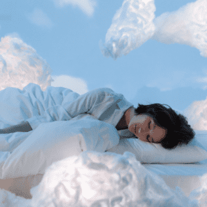 person with dark hair in white pajamas sleeping amongst the clouds in white sheets