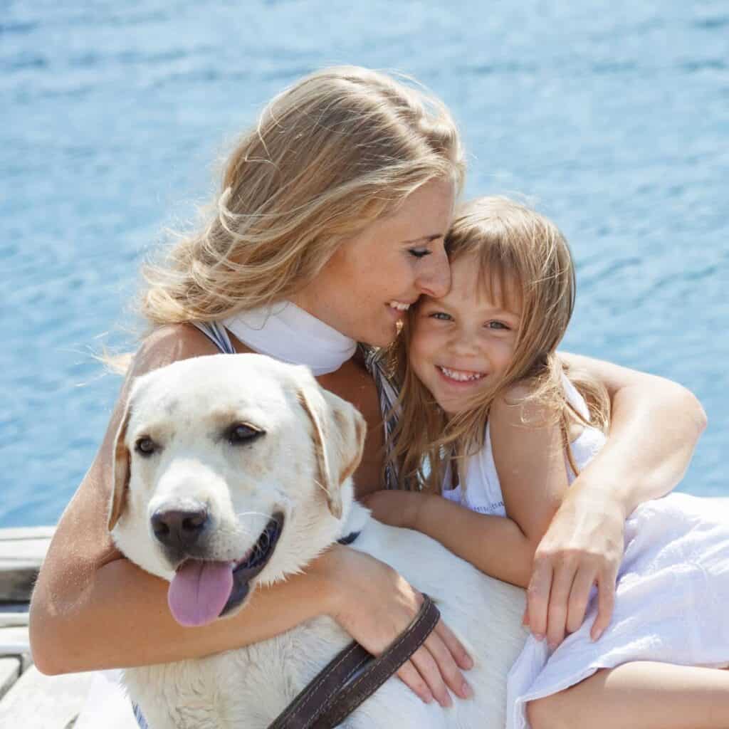 Woman, Labrador and small child on a boat hugging.
