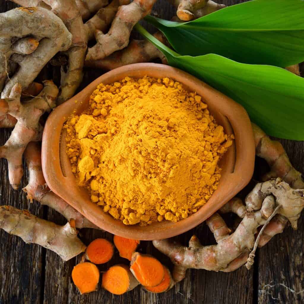 Picture of turmeric root, powder and sliced root on a flat lay black background.