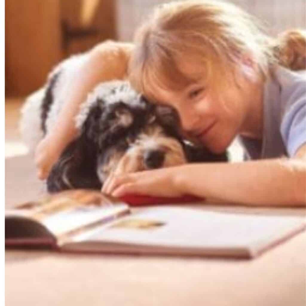 Black, white and grey shaggy dog reading with a girl with a ponytail on the floor.